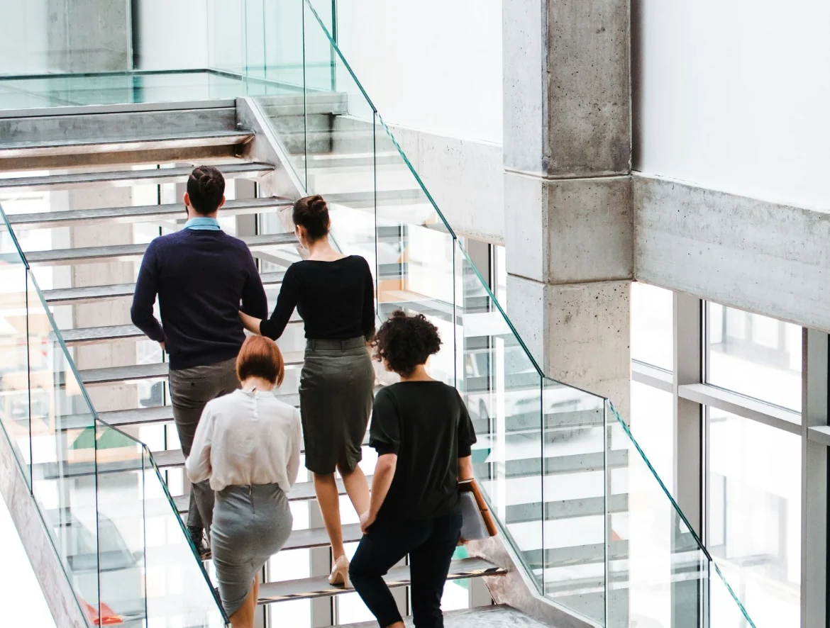 Vier Menschen gehen gemeinsam eine offene Treppe in einem modernen Gebäude hinauf